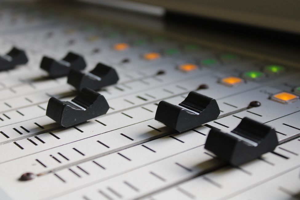 Detailed view of faders on an audio mixing console with illuminated buttons in a recording studio